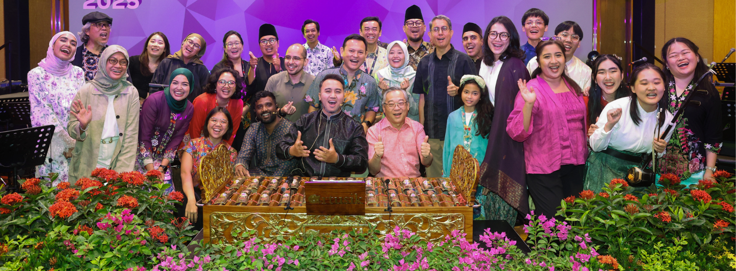 Group of people posing behind a gamelan instrument and flowers.